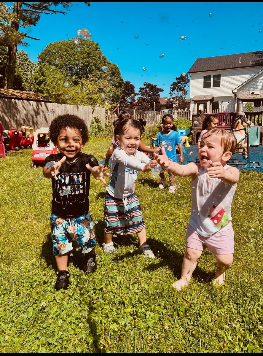 Three kids reaching for bubbles outside